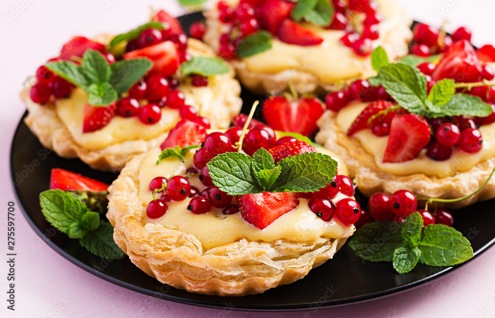 Tarts with strawberries, currant and whipped cream decorated with mint leaves. Tarts with strawberries, currant and whipped cream decorated with mint leaves.