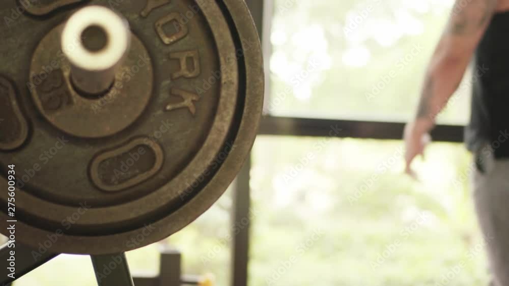 Sporty man with tattoos puts weights on bench press in gym close up Sporty man with tattoos puts weights on bench press in gym close up