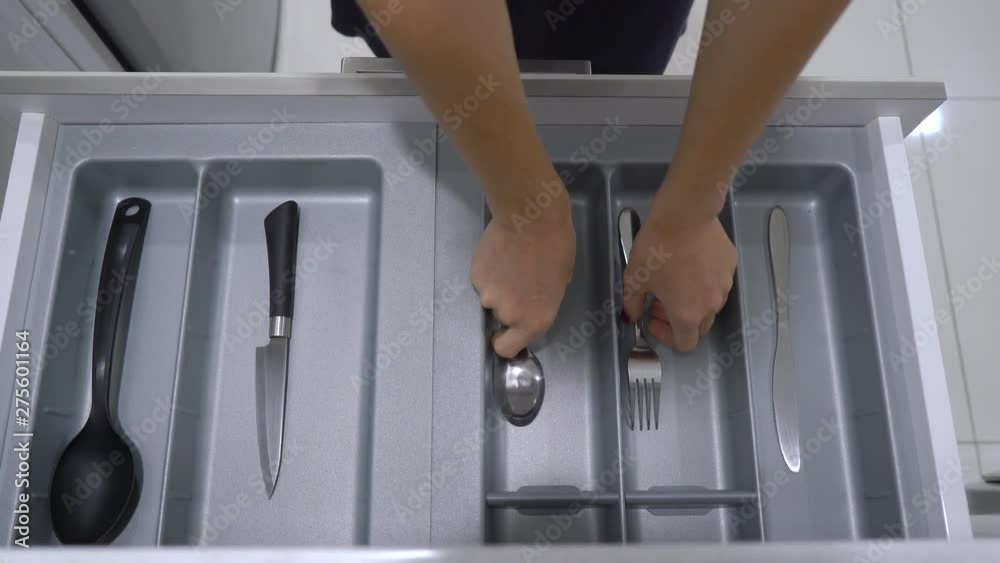 A woman walks to the kitchen cupboard and takes a spoon and fork from the drawer. In the box only two spoons and forks. Minimalism concept A woman walks to the kitchen cupboard and takes a spoon and fork from the drawer. In the box only two spoons and forks. Minimalism concept
