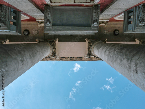 Stone columns (Entasis) of an old building. Beautiful capital (forms the topmost member of a column), balconies. Bottom view. Blue sky space. photo