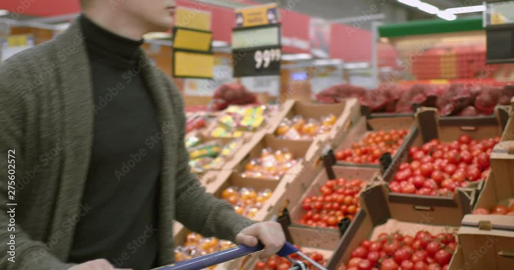 a young man walks through a supermarket with a cart in the vegetable department. He picks up yellow pepper. a young man walks through a supermarket with a cart in the vegetable department. He picks up yellow pepper.