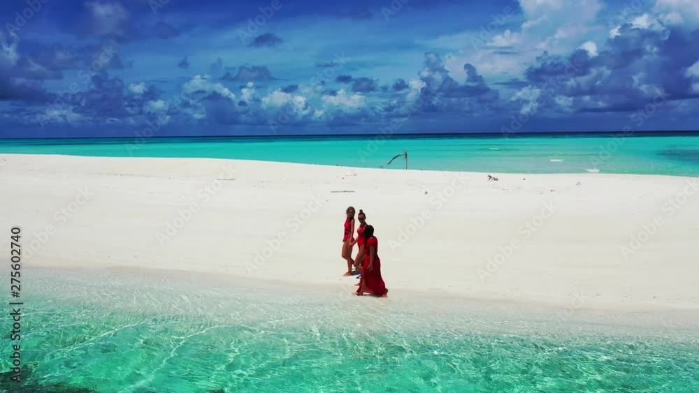Three young women walking along a white sandy beach. Clear water in front of it. A dramatic sky in the background. Truck left. Three young women walking along a white sandy beach. Clear water in front of it. A dramatic sky in the background. Truck left.