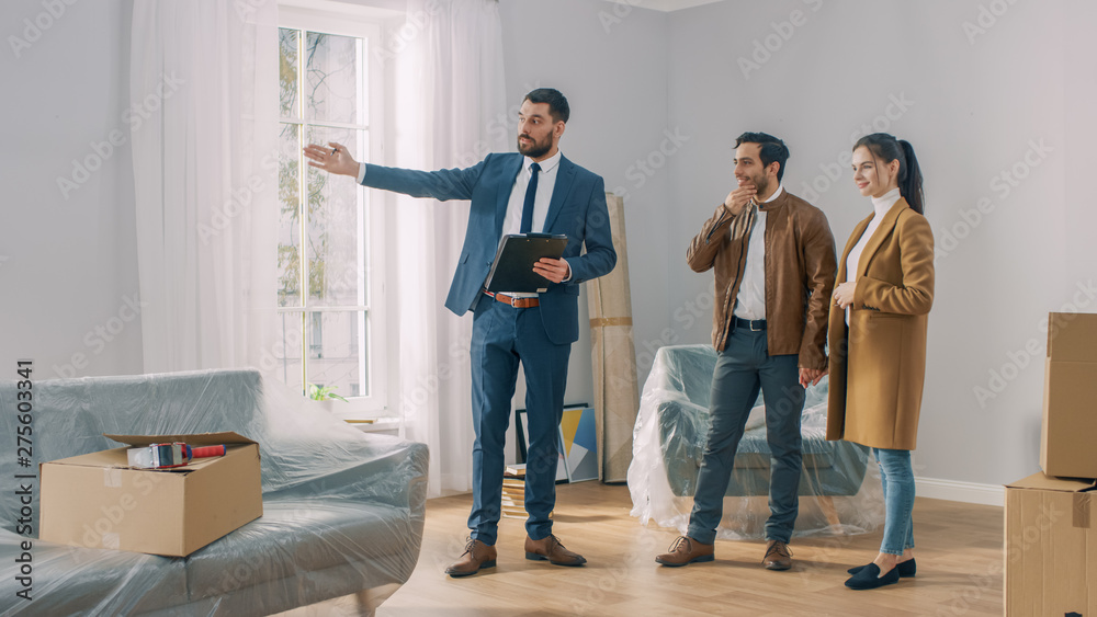 Fototapeta premium Professional Real Estate Agent Shows Bright New Apartment to a Young Couple. Successful Young Couple Ready to Become Homeowners. Spacious Bright Home with Big Windows.