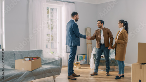 Real Estate Agent Shows Bright New Apartment to a Young Couple. Successful Young Couple Becoming Homeowners, Seal the Deal with Real Estate Broker by Handshake. Spacious Bright Home with Big Windows.