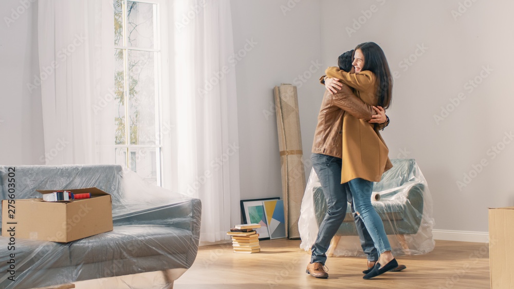 Happy and Excited Young Couple Look Around In Wonder at their Newly Purchased / Rented Apartment. Beautiful People Happily Embracing. Big Bright Modern Home with Cardboard Boxes Ready to Unpack. Happy and Excited Young Couple Look Around In Wonder at their Newly Purchased / Rented Apartment. Beautiful People Happily Embracing. Big Bright Modern Home with Cardboard Boxes Ready to Unpack.