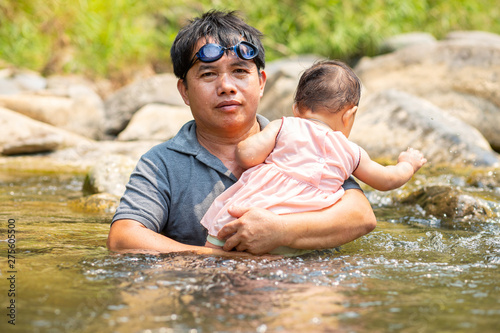 Asian man wearing goggles carrying his baby girl in water