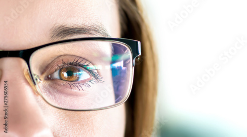 Close up of eye and woman wearing glasses. Optometry, myopia or laser surgery concept. Brown eyed girl with spectacles and eyeglasses. Macro portrait of face and specs. Light reflection on lens. photo
