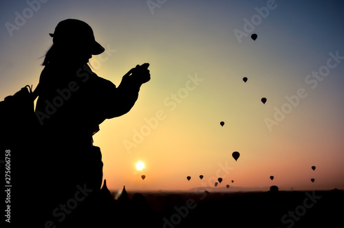 silhouette woman traveler take photo view sunrise with many hot air balloons above Bagan in Myanmar.