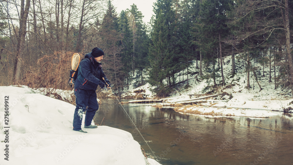 Angler with a rod on the river bank. Fishing for trout. Winter spinning.
