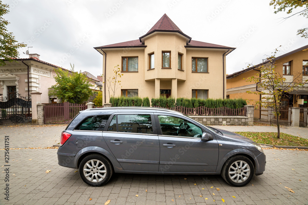 New expensive gray car parked in paved parking lot in front of big two story cottage. Luxury and prosperity concept.