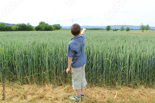 Fotografie boy in a denim shirt and shorts stands at the edge of a green field with a rich