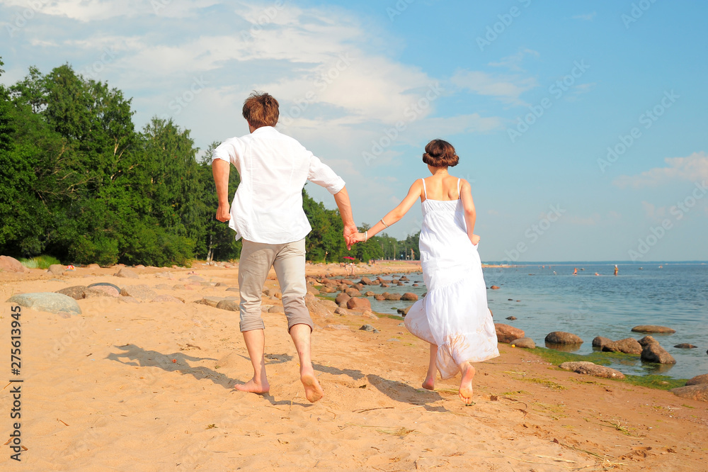 young loving couple in white running on the sand near the sea young loving couple in white running on the sand near the sea