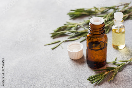 Rosemary essential oil in a glass bottle with fresh branch rosemary herb on grey table for spa,aromatherapy and bodycare.Copy space.