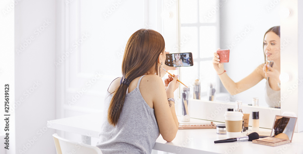 Amazing young woman doing her makeup in front of mirror. Portrait of beautiful girl near cosmetic table Amazing young woman doing her makeup in front of mirror. Portrait of beautiful girl near cosmetic table