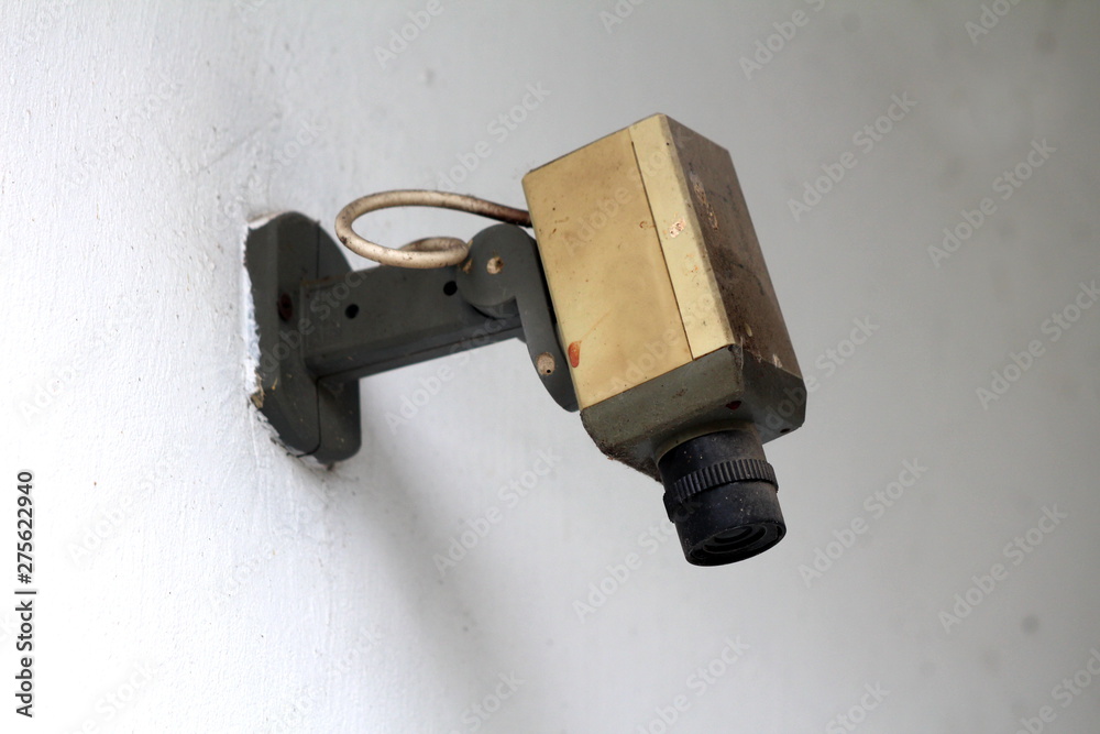 Vintage retro small black and white security camera mounted on building wall and covered with thick layer of dust on warm spring day