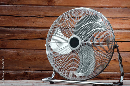 Large tabletop ventilator on the table against the background of a wooden wall. The concept of heat, hot weather, air conditioning