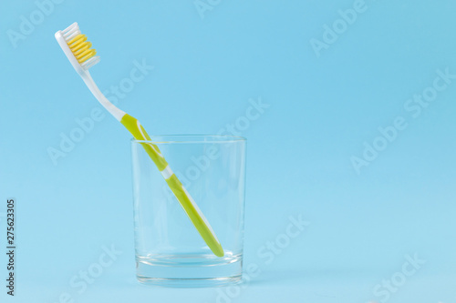Oral hygiene. green toothbrush in a glass on a gentle blue background. space for text