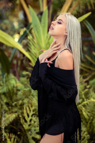 Luxury young blonde in a black shirt is smiling at the camera. Background of palm trees.