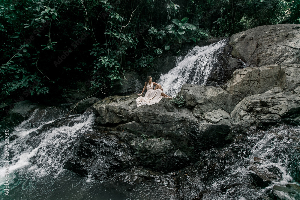 Portrait of the young Caucasian woman enjoying in front of a waterfall in an white evening dress Portrait of the young Caucasian woman enjoying in front of a waterfall in an white evening dress