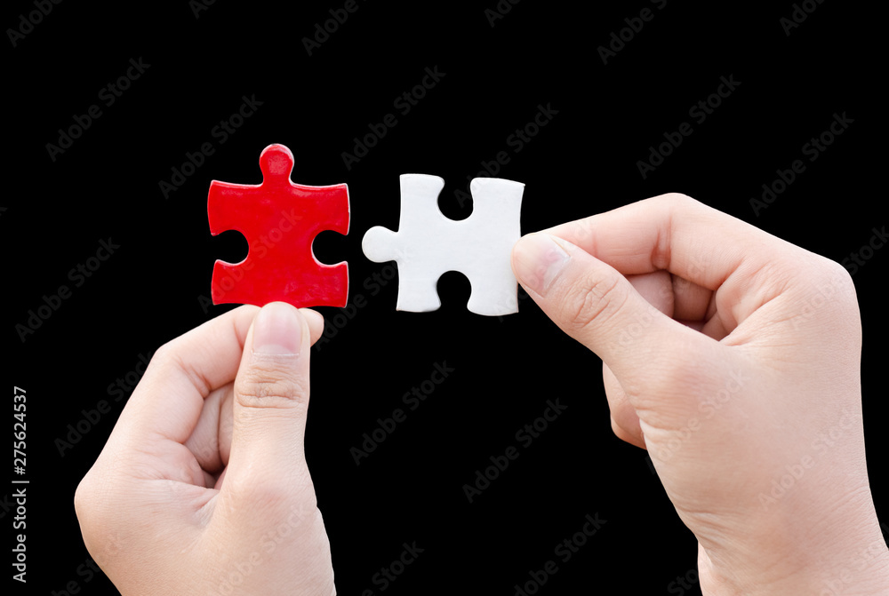 hands holding piece of red and white jigsaw puzzle on black background. teamwork concept hands holding piece of red and white jigsaw puzzle on black background. teamwork concept