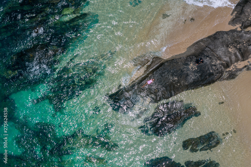 Fototapeta premium Portret moda styl życia na zewnątrz ładna dziewczyna leżącego na dużych kamieniach w morzu. Ubrana w stylową krótką różową sukienkę. Samotny. Sztuka fotograficzna. Twórczy. Widok z góry