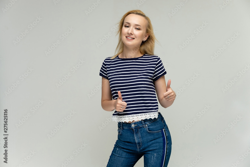 Portrait of a pretty interesting blonde girl on a white background in jeans and a striped blue t-shirt. Standing in front of the camera, smiling, showing hands. Shows a lot of emotions. Portrait of a pretty interesting blonde girl on a white background in jeans and a striped blue t-shirt. Standing in front of the camera, smiling, showing hands. Shows a lot of emotions.