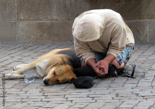 A homeless man with a dog asks for alms on his knees and hooded