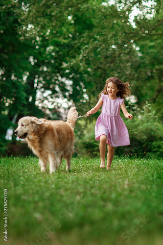 Little girl playing with a golden retriever, outdoor summer