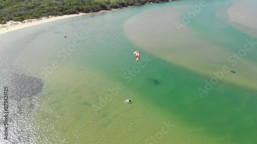 Aerial pan of kite surfer in clear green river estuary in light wind.