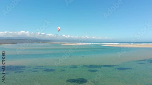 Aerial rise and reveal of kite surfer in clear green river estuary in light wind.