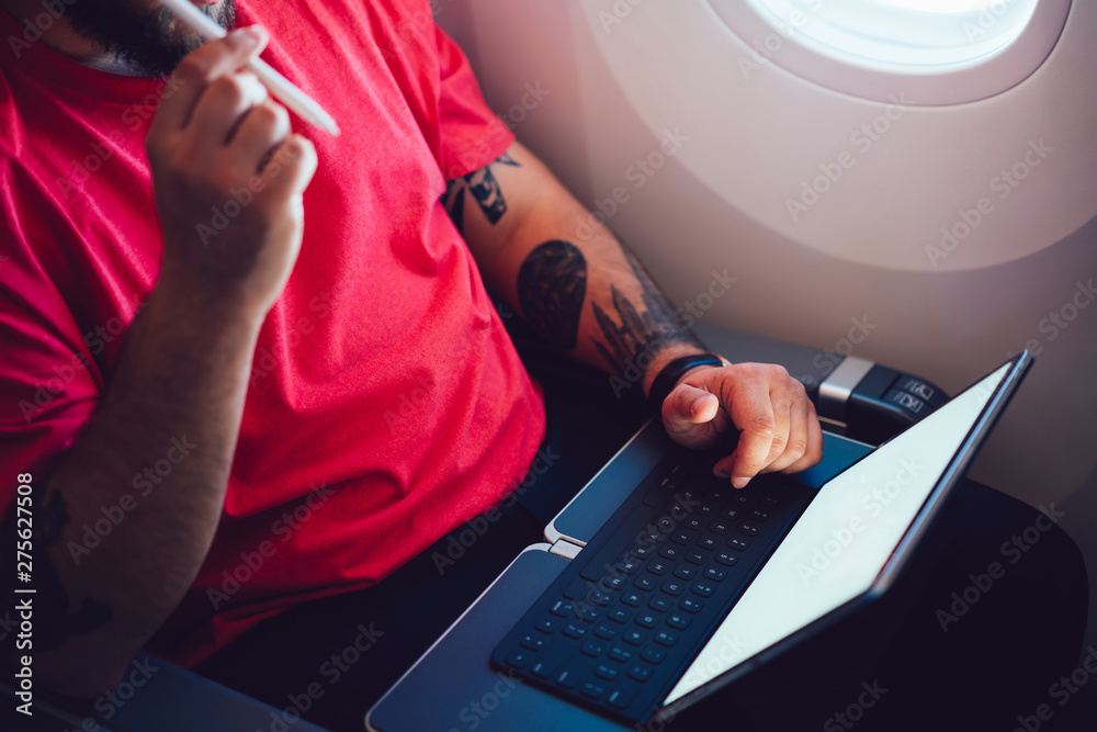 Young man flight passenger connecting to wireless internet on board with touch pad while sitting next to aircraft cabin window. Mock up blank screen for web template, thinking on work planning