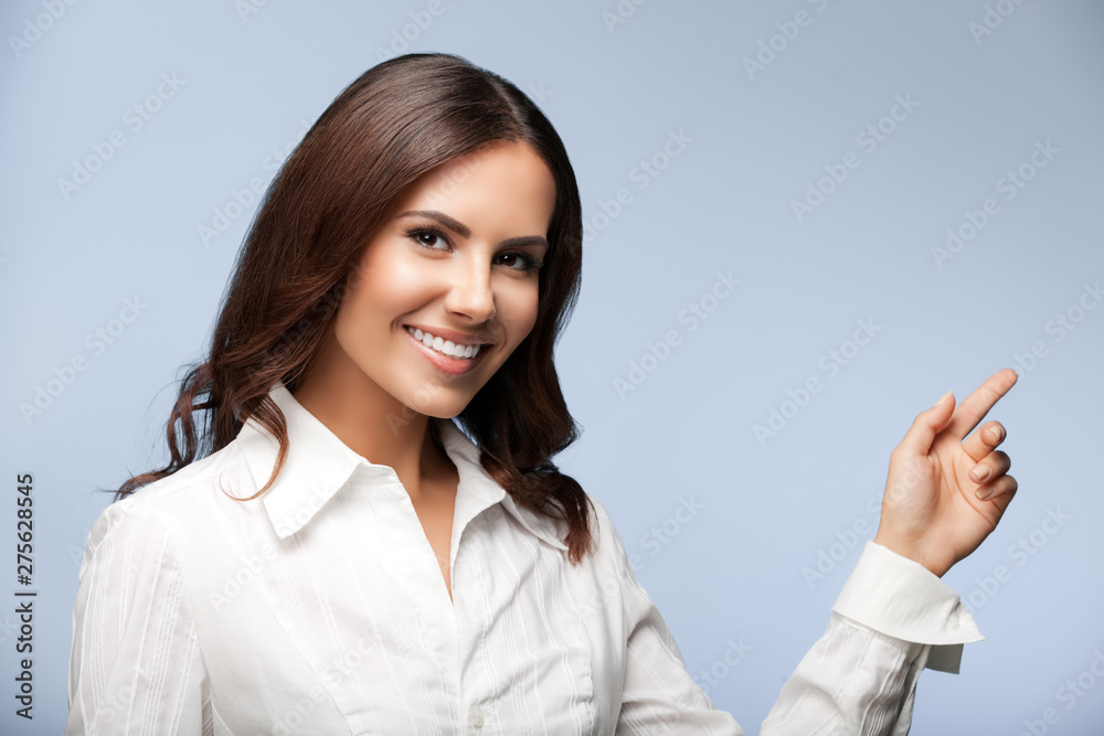 Portrait of happy smiling businesswoman, showing something or blank copyspace area for slogan or text message, over grey background Portrait of happy smiling businesswoman, showing something or blank copyspace area for slogan or text message, over grey background