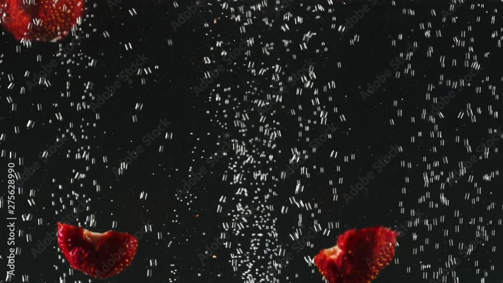 Strawberry halves falling into the water with bubbles on black background. Fresh berries in the water. Organic berry, fruit, healthy food. Slow motion. Strawberry halves falling into the water with bubbles on black background. Fresh berries in the water. Organic berry, fruit, healthy food. Slow motion.