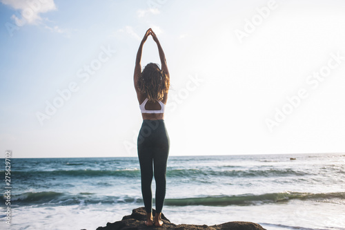 Back view of young woman increases body awareness while doing tadasana pose near ocean coastline enjoying time for recreating soul, concept of healthy lifestyle and harmony with yoga meditation photo