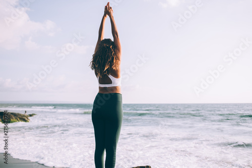 Back view of young woman doing tadasana for relaxes centers attention and sharpens concentration, female enjoying time for practising yoga on coastline training balance and harmony on nature photo