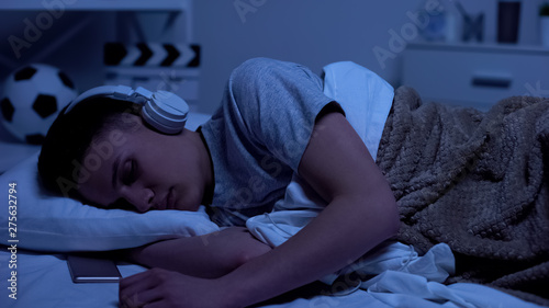 Obraz na plátně Male teenage boy fallen asleep in headphones, overworked student relaxing