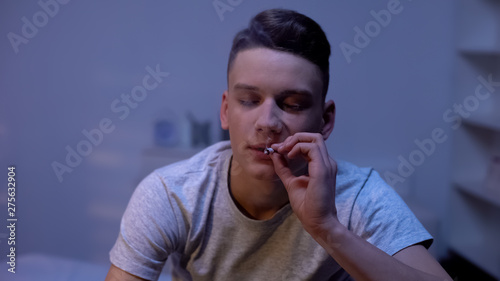 Male teenager smoking weed joint, evening at home, awkward age experiment
