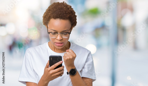 Young african american woman using smartphone over isolated background annoyed and frustrated shouting with anger, crazy and yelling with raised hand, anger concept