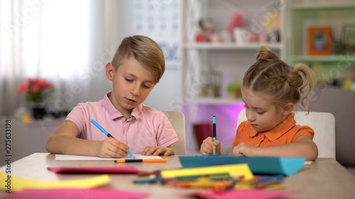 Adorable boy and girl drawing with pencils  sitting at table  kindergarten