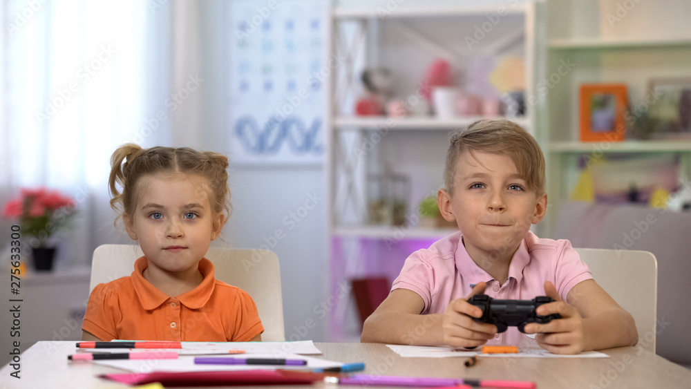 Boy playing video game using console, sister looking at screen, having fun Boy playing video game using console, sister looking at screen, having fun