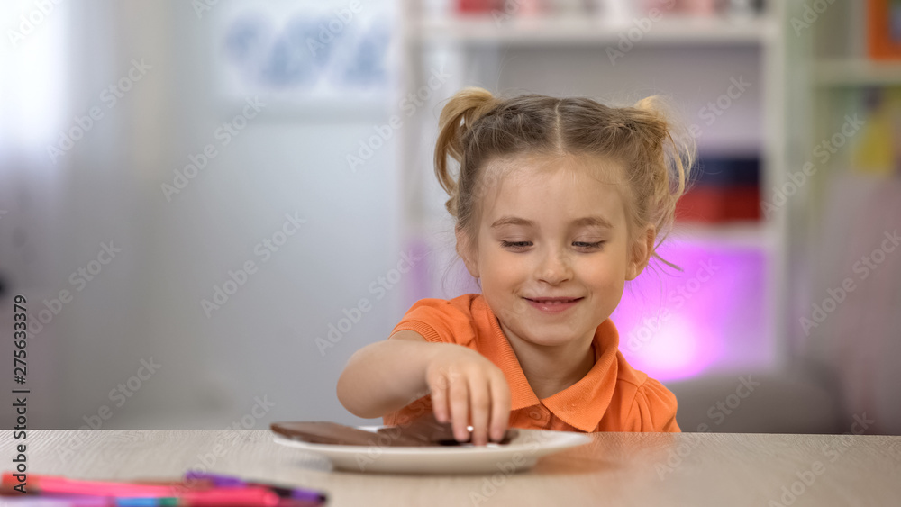 Female kid secretly taking chocolate from white plate on table, sugar overdose