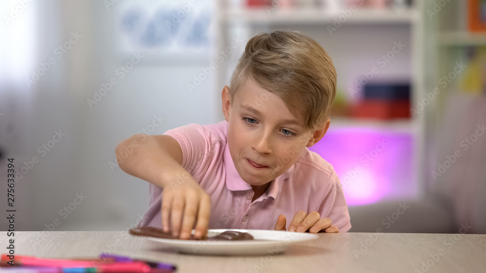 Schoolboy secretly taking chocolate from white plate on table, sweet dessert Schoolboy secretly taking chocolate from white plate on table, sweet dessert