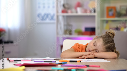 Adorable schoolgirl sleeping on desk, color pencils and paper on table education