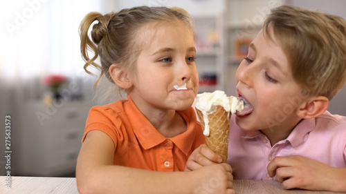 Adorable boy and girl eating ice-cream together, sitting at home table, food
