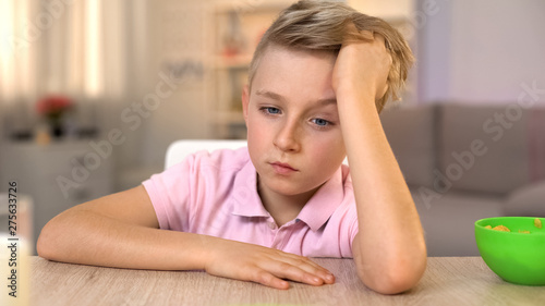 Pensive boy sitting at table, thinking about problems at school, bullying