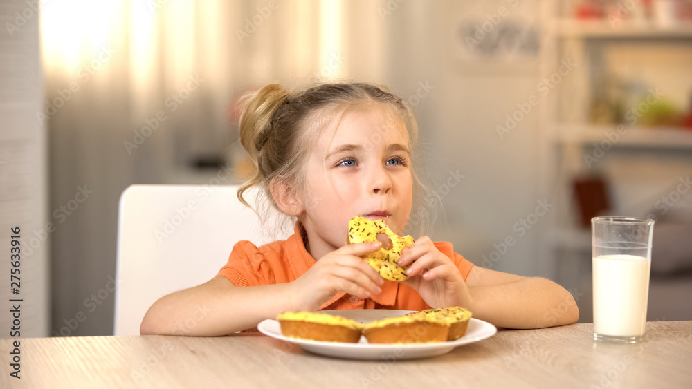 Female child eating tasty donut, milk glass on table, sweet snack, nutrition Female child eating tasty donut, milk glass on table, sweet snack, nutrition