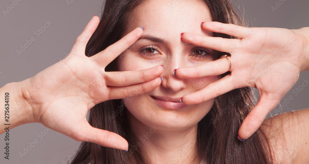 Obraz premium Young woman looking through fingers and hand as a symbol of bribery, cheating, corruption and political manipulation.