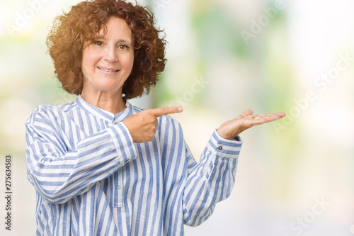 Beautiful middle ager senior woman wearing navy shirt over isolated background amazed and smiling to the camera while presenting with hand and pointing with finger.