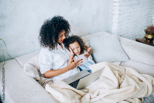 Woman with girl relaxing on sofa with laptop