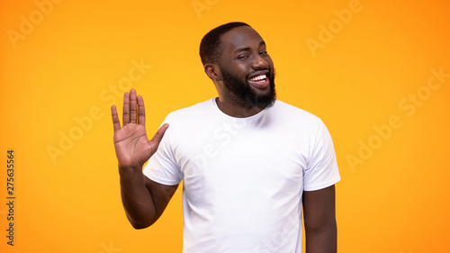 Affable young black man showing palm, waving hand neighborly yellow background photo